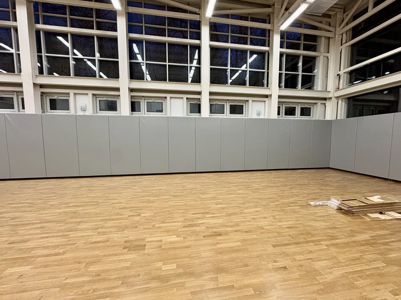 Готовая стена с серыми защитными протекторами под большими окнами спортзала