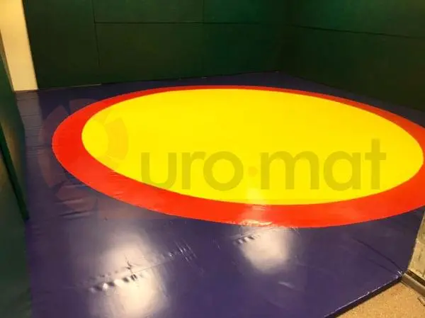 Борцовский ковёр синего цвета с жёлтым кругом и красной полосой в частном зале с зелёными стеновыми протекторами