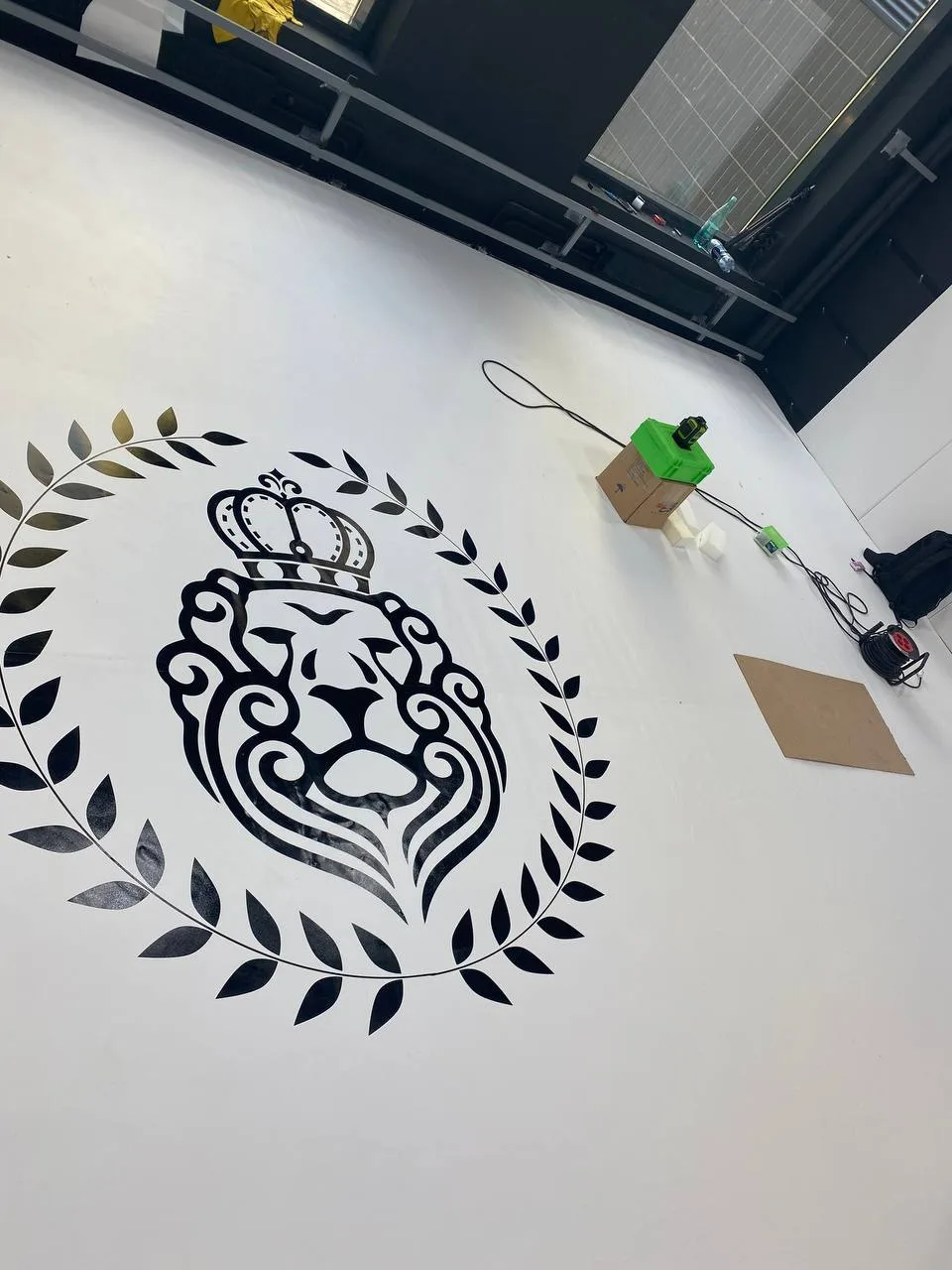 Крупный план белого борцовского ковра с чёрно-золотым логотипом льва школы «Седьмой император»