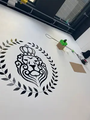 Крупный план белого борцовского ковра с чёрно-золотым логотипом льва школы «Седьмой император»