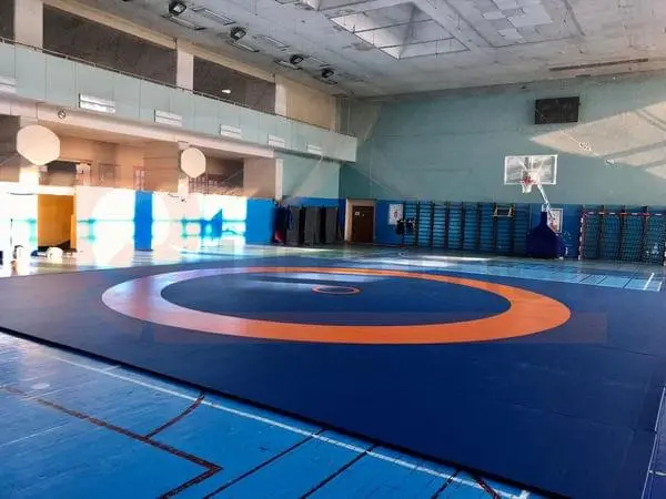 Борцовский ковёр синего и оранжевого цвета в школьном спортзале, вид на круг для борьбы