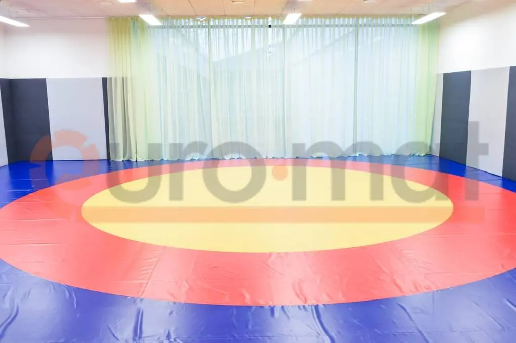 Борцовский ковёр с жёлтым центром и красно-синими кольцами, зелёные шторы и стеновые протекторы