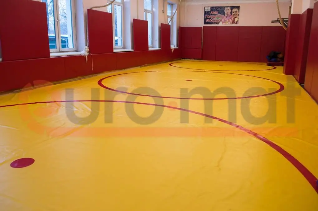 Жёлтый борцовский ковёр с красными кругами и красные стеновые протекторы, вид от окон