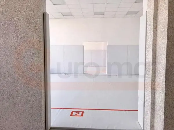 Вид через дверной проём на борцовский зал в Анапе с белым ковром, красной разметкой и стеновыми протекторами