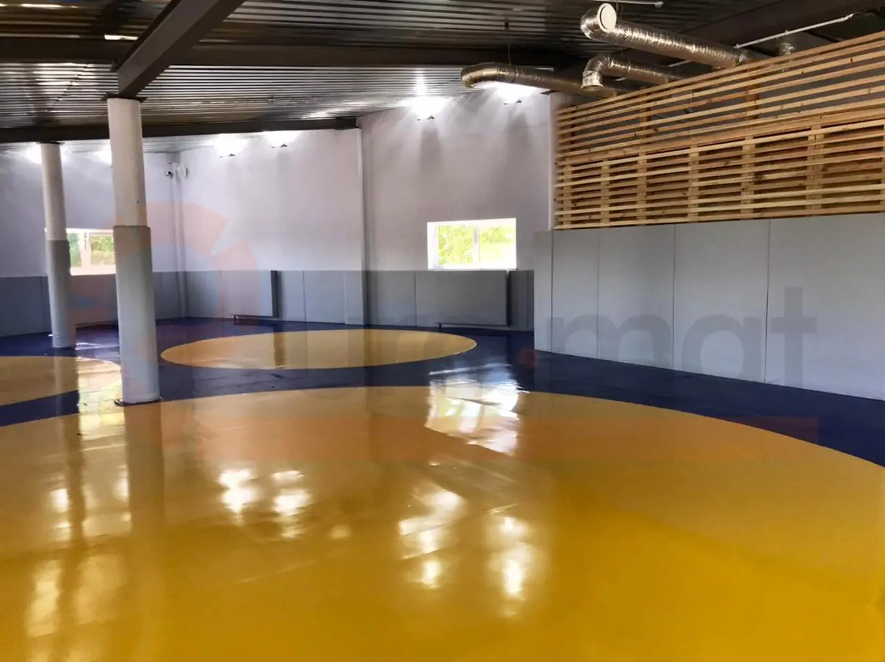 Борцовский ковёр с жёлтым кругом крупным планом и стеновые протекторы с деревянной решёткой в зале борьбы