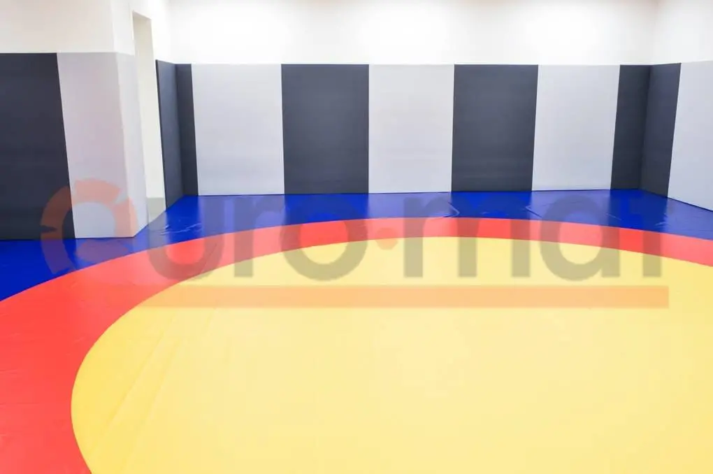 Борцовский ковёр с жёлтым, красным и синим кругами и тёмно-серые стеновые протекторы в зале борьбы