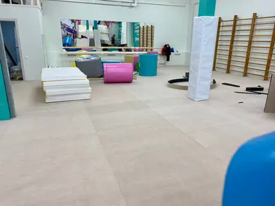 Бежевый ролл-гимнаст в зале с гимнастическими модулями и протектором на колонне