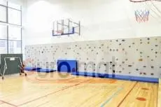 Синие гимнастические маты у скалодрома в школьном спортзале с баскетбольными кольцами