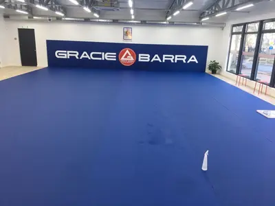 Широкий вид зала Gracie Barra с синим ролл-матом на полу и протектором с надписью на стене