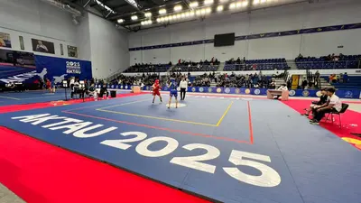 Поединок ушу на синем ролл-мате, зрители на трибунах, надпись AKTAU 2025