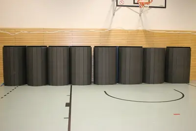 Свёрнутые чёрные ролл-маты у стены немецкого спортзала в компактном хранении