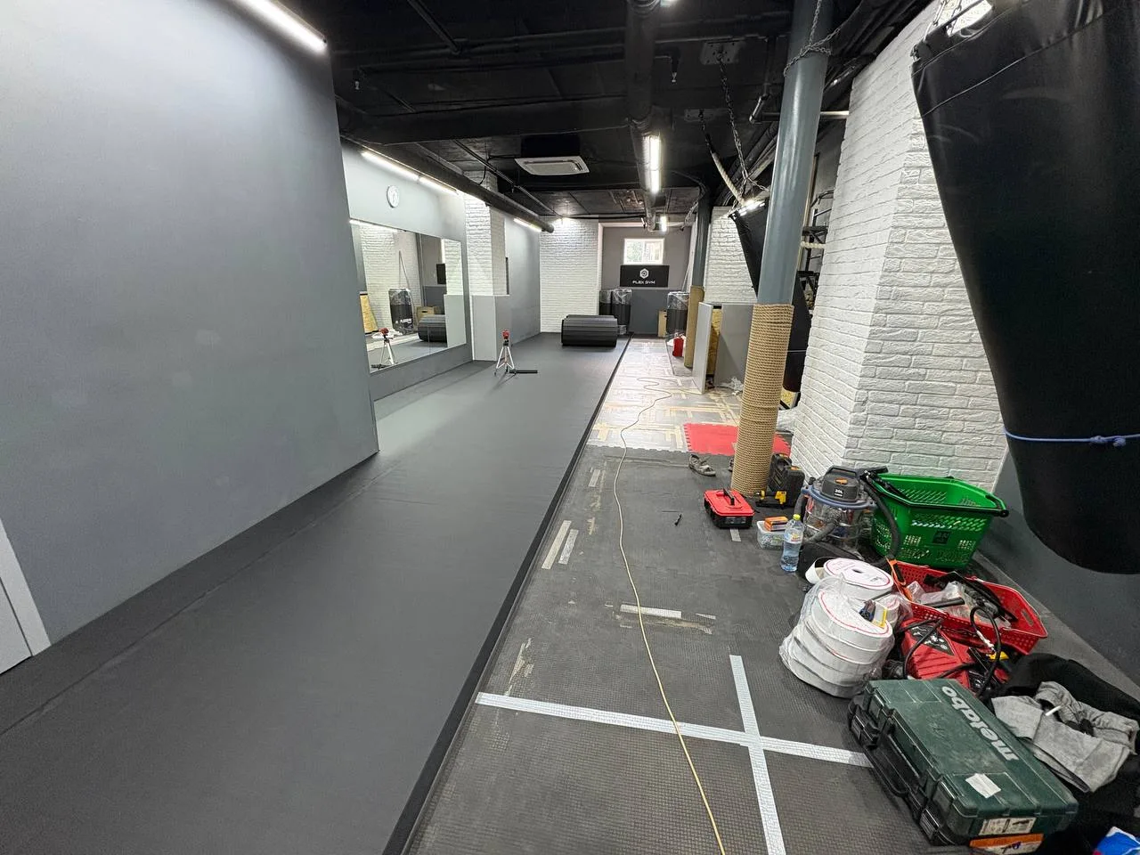 Укладка серого ролл-мата в тёмном зале Flex Gym Липецк с серыми стеновыми протекторами и грушей