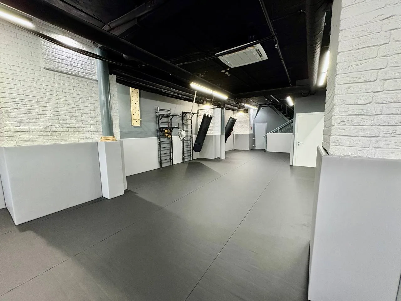 Тренировочный зал с серым ролл-матом, боксёрскими грушами и протекторами