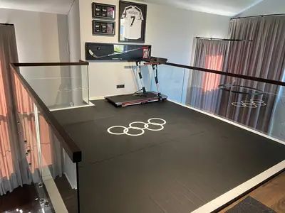 Черный ролл-мат с олимпийскими кольцами на антресольном этаже домашнего спортзала Никиты Нагорного