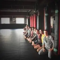 Чёрные ролл-маты в зале MMA Kegi, бойцы сидят у боксёрских мешков