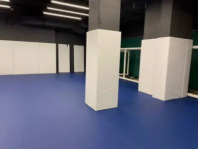 Белые протекторы на двух бетонных колоннах, синий пол и клетка MMA в зале борьбы в Москве