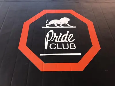 Крупный план логотипа Pride Club — лев в красной октагональной рамке на чёрном ролл-мате