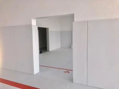 Белые стеновые протекторы на дверном проёме, за ним второй зал с белым ковром