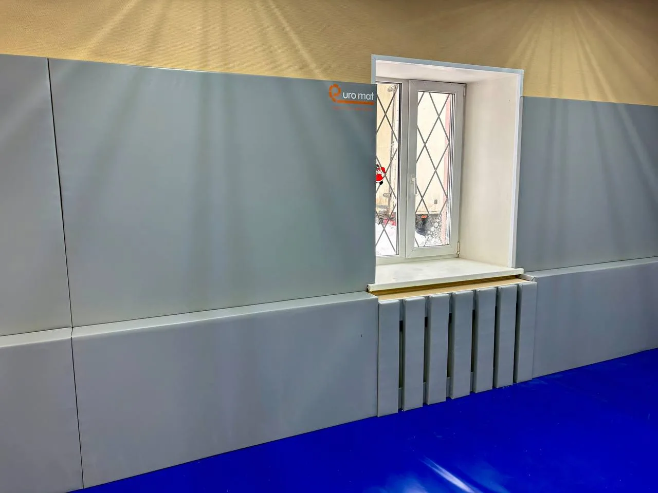 Серые стеновые протекторы ЕВРОМАТ вокруг окна и радиатора в готовом зале борьбы Красный Электрик