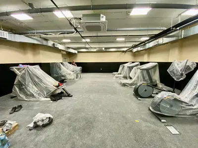 Чёрные стеновые протекторы на стенах тренажёрного зала, тренажёры укрыты плёнкой