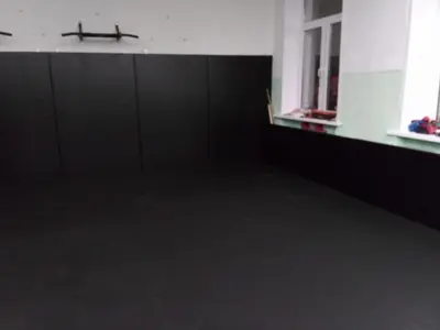 Угол зала единоборств с черными протекторами и ролл-матом, боксерские перчатки на подоконнике