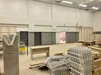 Широкий вид школьного спортзала с серыми протекторами, баскетбольными кольцами и стройматериалами