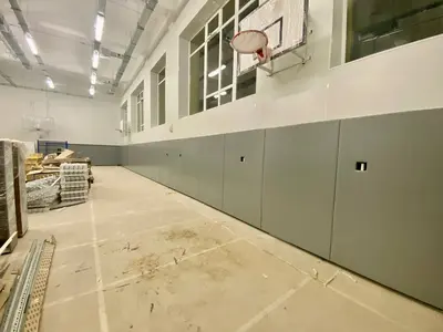 Серые протекторы на длинной стене с баскетбольным кольцом в школьном спортзале