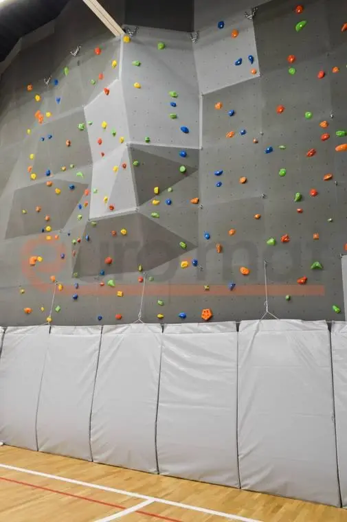 Белые стеновые протекторы под скалодромом с цветными зацепами в школьном спортзале