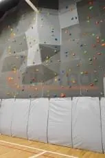 Белые стеновые протекторы под скалодромом с цветными зацепами в школьном спортзале