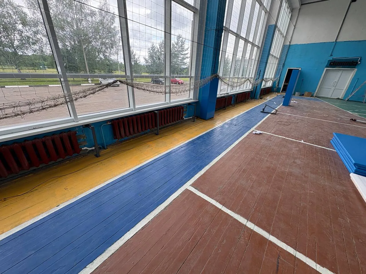 Вид на окна спортзала с радиаторами отопления и спортивной разметкой на полу