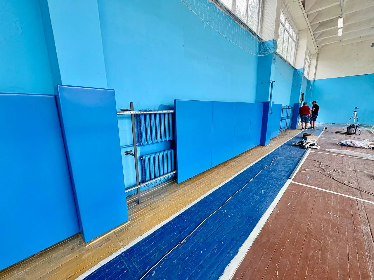 Монтажники устанавливают синие стеновые протекторы на стены спортзала колледжа