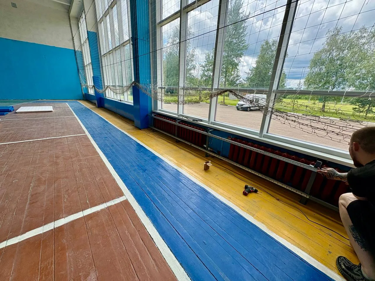 Монтажник устанавливает каркас для стенового протектора рядом с окном и радиатором