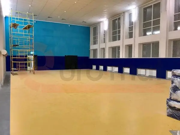 Синие стеновые протекторы по периметру зала единоборств, жёлтый спортивный пол, строительные леса