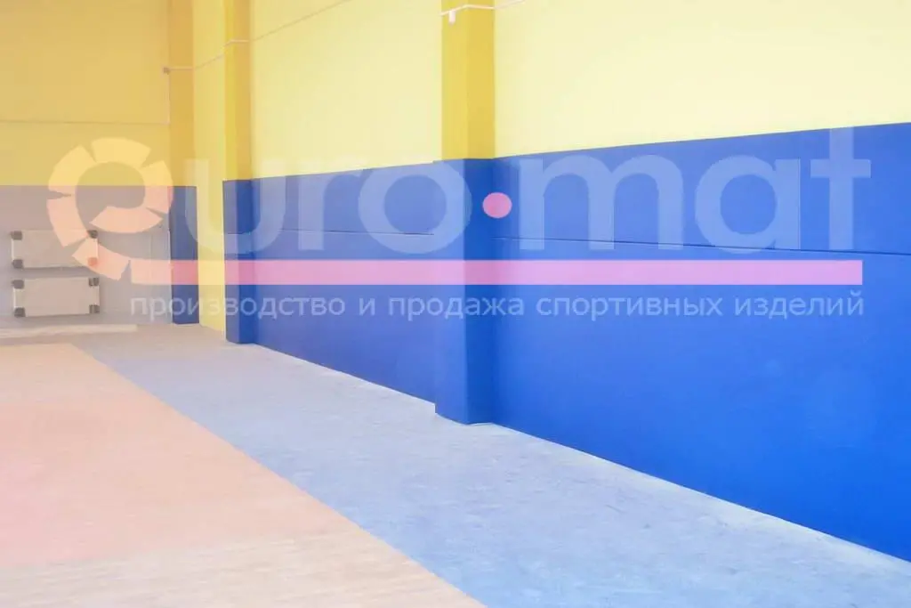 Синие стеновые протекторы вдоль стены спортзала с жёлтыми колоннами, вид сбоку