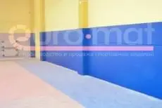 Синие стеновые протекторы вдоль стены спортзала с жёлтыми колоннами, вид сбоку