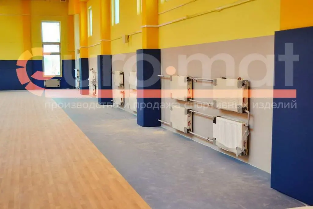 Синие стеновые протекторы между жёлтыми колоннами в спортзале с радиаторами на стене