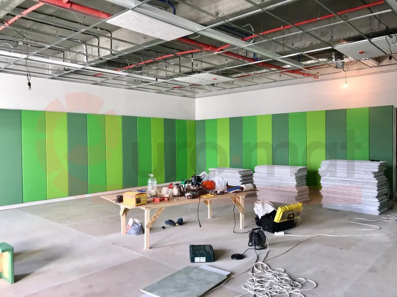 Монтаж зелёных стеновых протекторов разных оттенков в спортзале, стопки панелей и инструменты