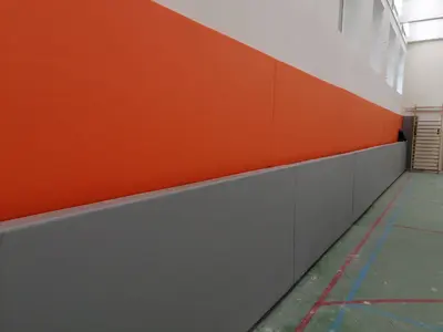 Длинная стена с оранжево-серыми двухуровневыми протекторами в спортзале Люберцы, зелёный пол с разметкой