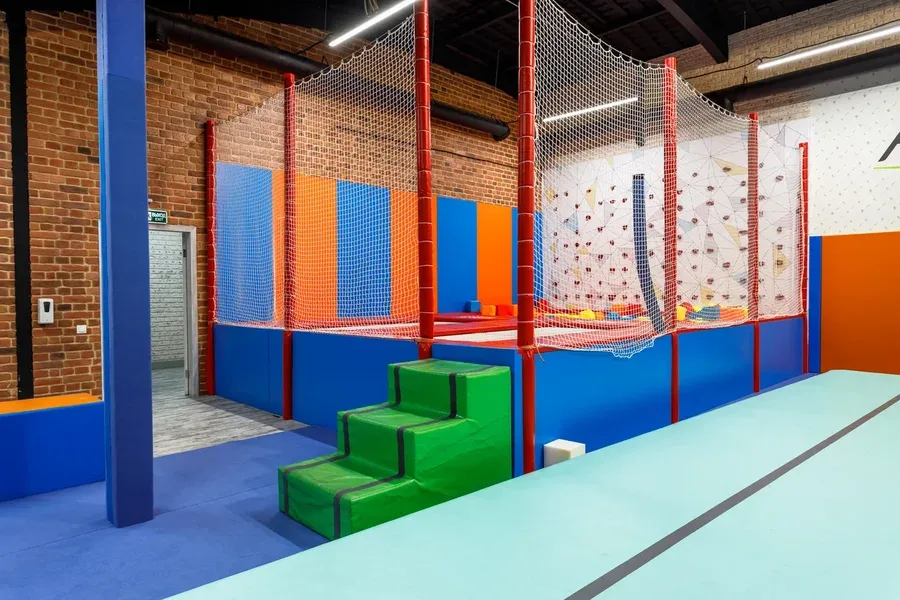 Батутная зона Park Arena с синими и оранжевыми стеновыми протекторами на стенах и зелёными поролоновыми ступенями
