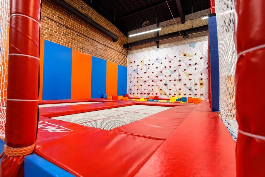 Вид через батутную сетку на синие и оранжевые стеновые протекторы, скалодром с цветными кубиками