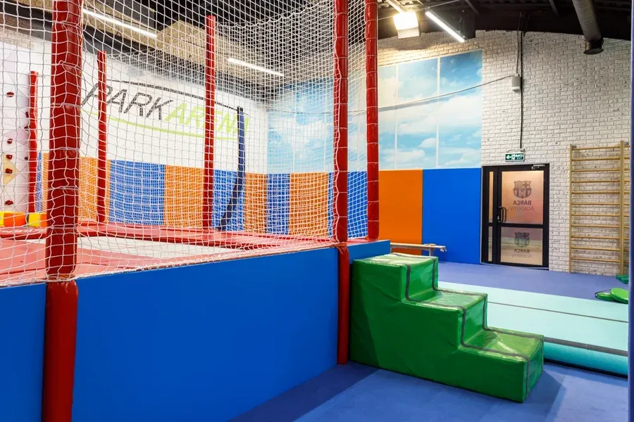 Батутная зона Park Arena через защитную сетку с синими стеновыми протекторами и зелёными поролоновыми ступенями