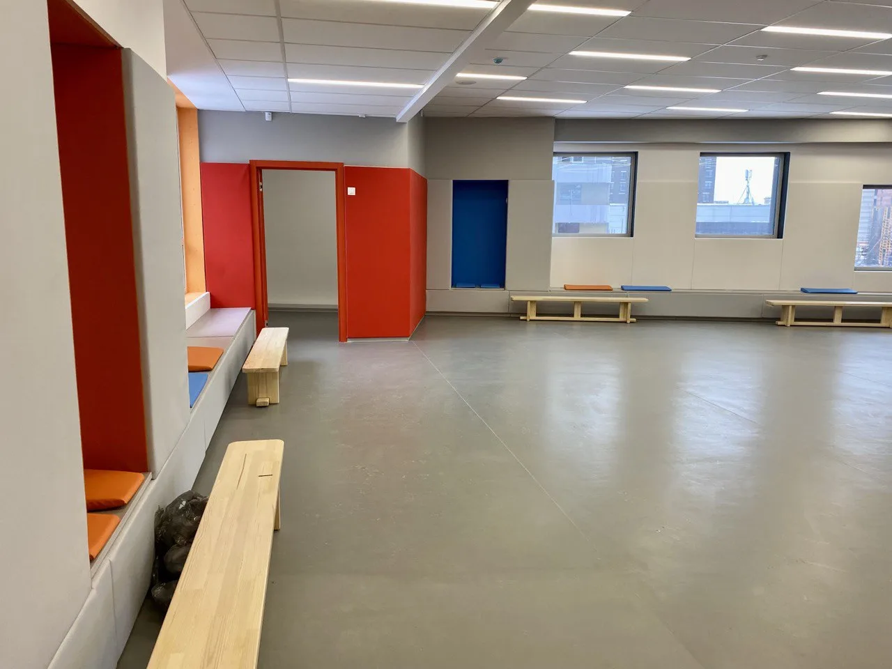 Серо-белые стеновые протекторы с оранжевым акцентом и мягкая скамья в зале Новой школы