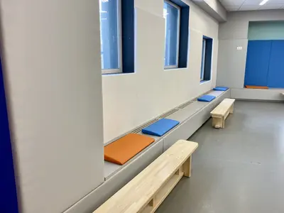 Мягкие скамьи и серо-белые протекторы вдоль стены в спортзале Новой школы
