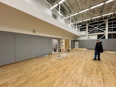 Серые протекторы вдоль стены, балкон с перилами сверху, рабочий осматривает монтаж, паркет