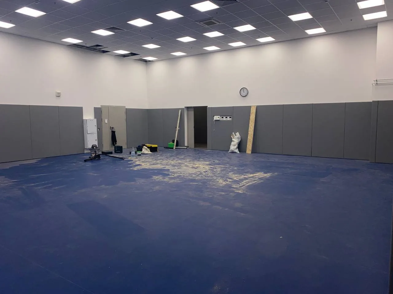 Панорамный вид тренировочного зала: боксёрский ринг, синие татами, серые стеновые протекторы