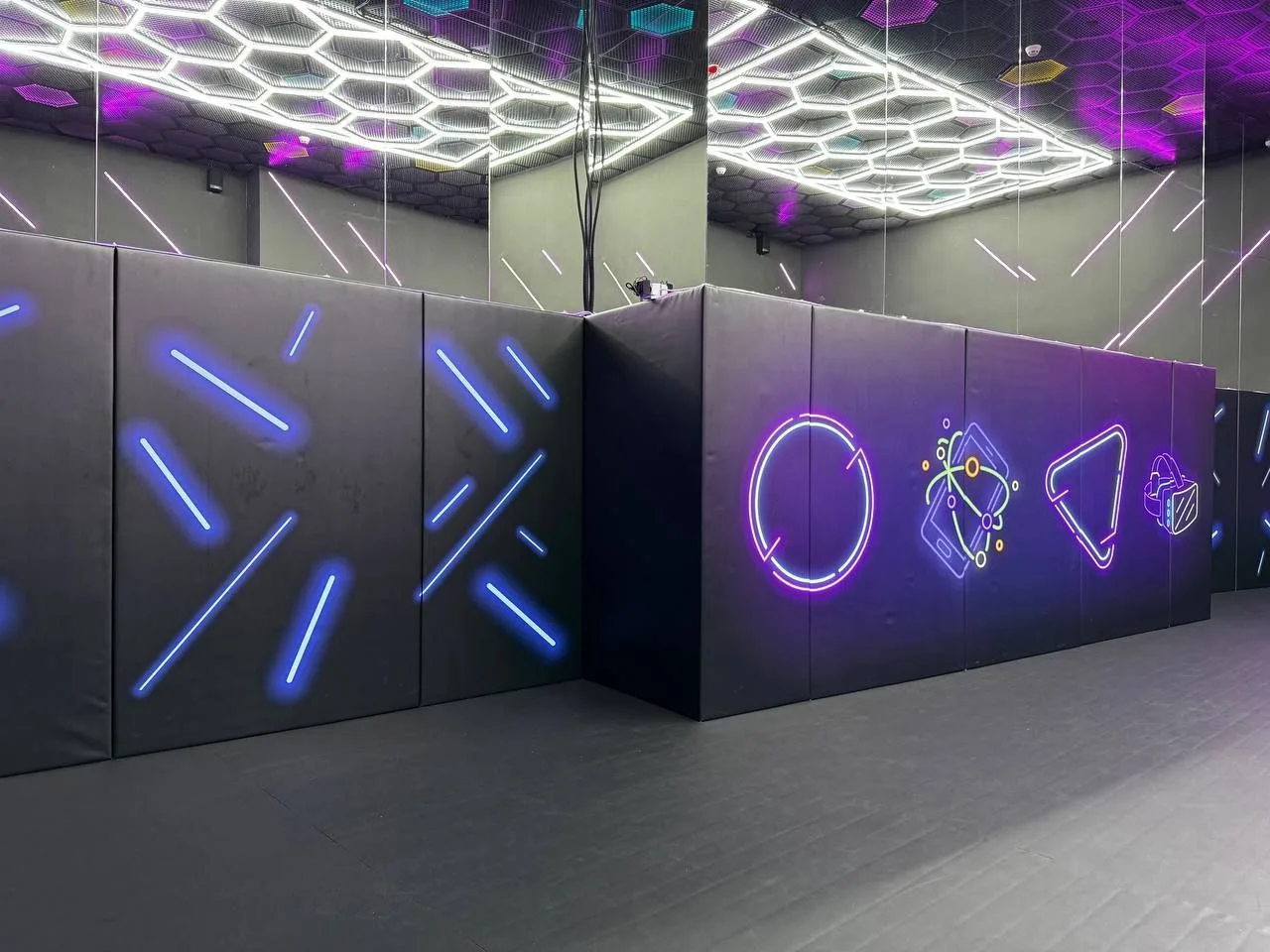 Стильная игровая зона с чёрными стеновыми протекторами, неоновым декором и шестиугольными светильниками