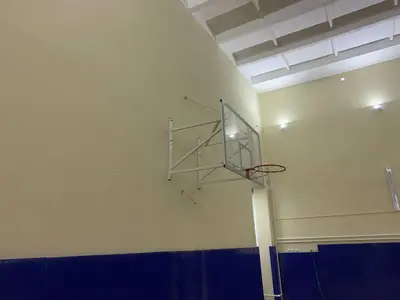 Складной баскетбольный щит над синими стеновыми протекторами в школьном спортзале Няндома