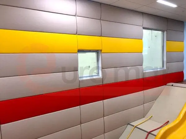 Бежевые стеновые протекторы с жёлтыми и красными полосами вдоль стены детского зала с окнами