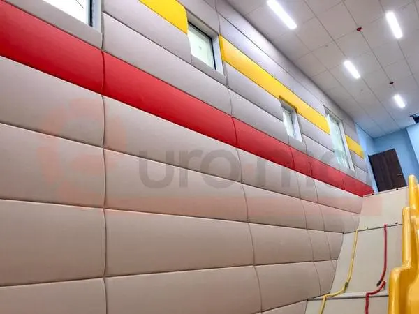 Длинная стена с бежевыми, красными и жёлтыми стеновыми протекторами в высоком детском спортзале школы