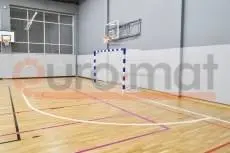 Белые стеновые протекторы вдоль стен школьного спортзала с баскетбольным щитом и гандбольными воротами